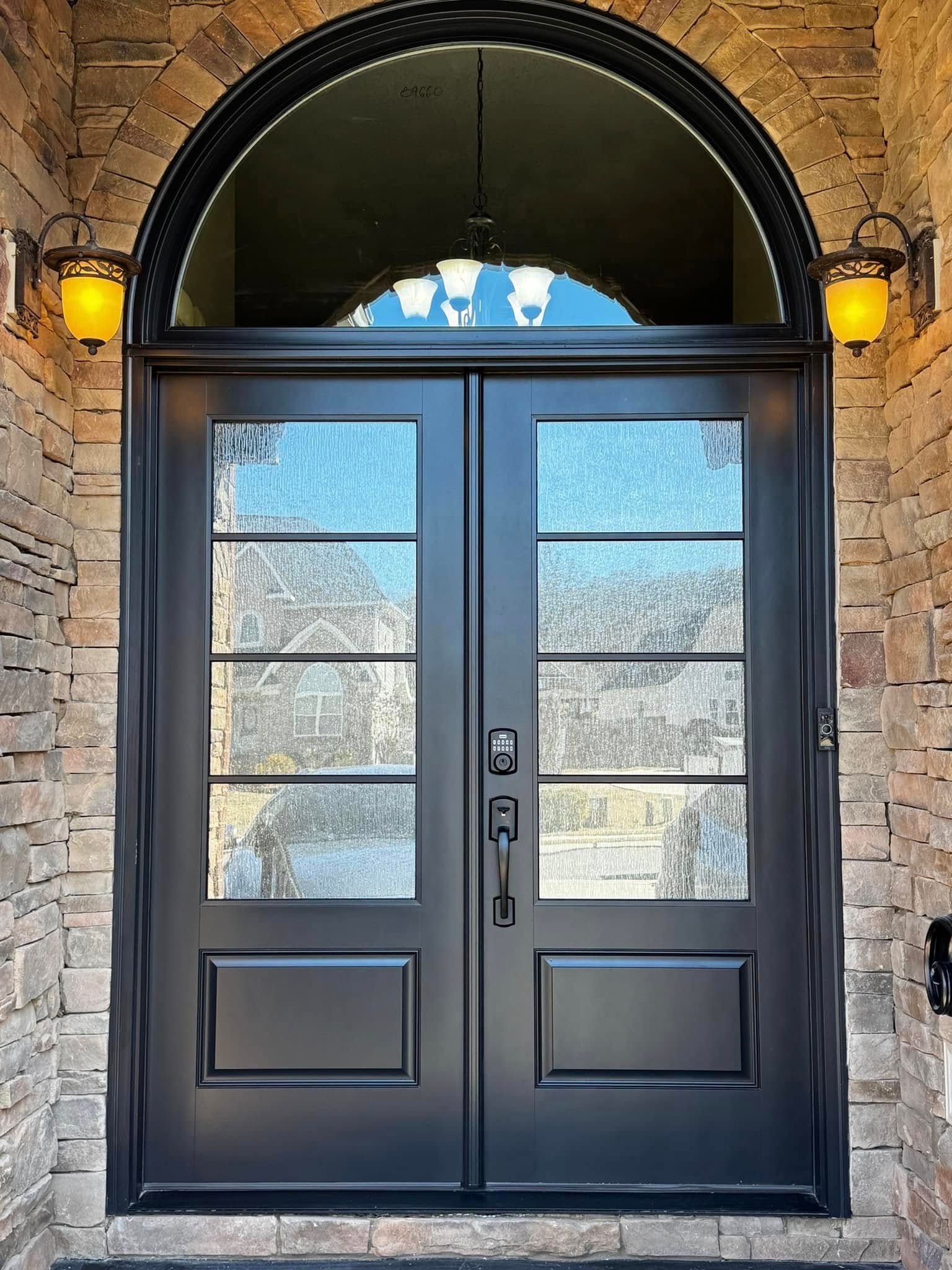 Black double doors with glass panels and sidelights under an arched doorway with stone brick.
