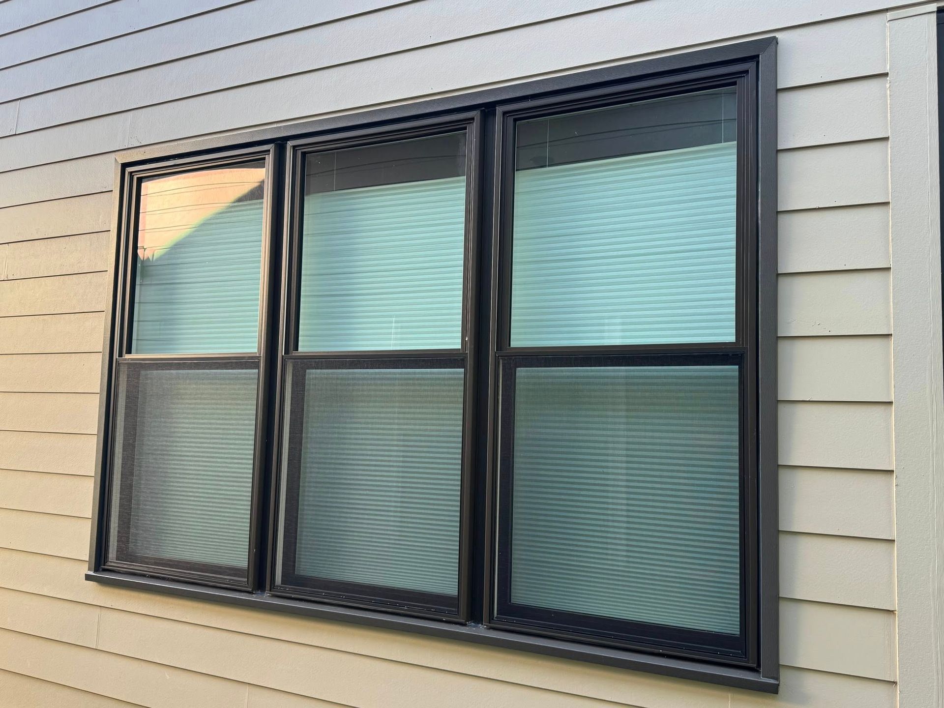 Triple-pane window with black frames set in light tan siding. One pane is partially open.