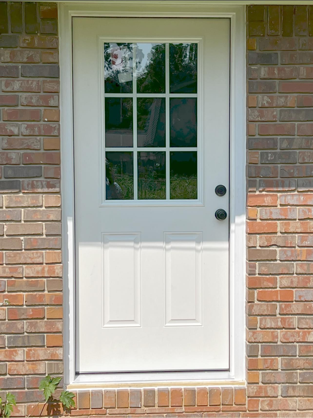 White door with glass pane, black handle, set in brick wall.