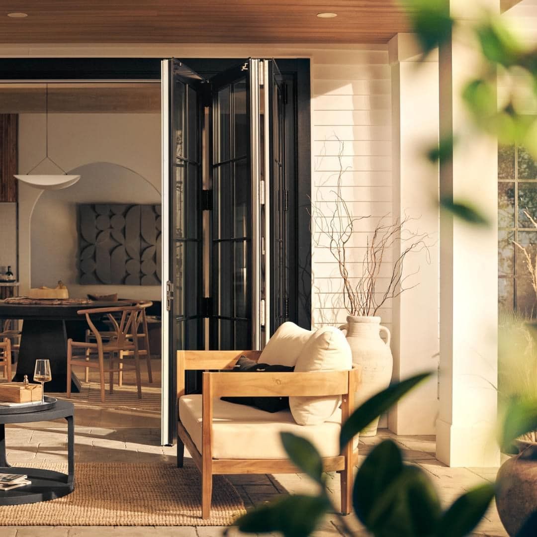 Outdoor patio with open folding doors leading to a dining room, wooden chair, and plants.
