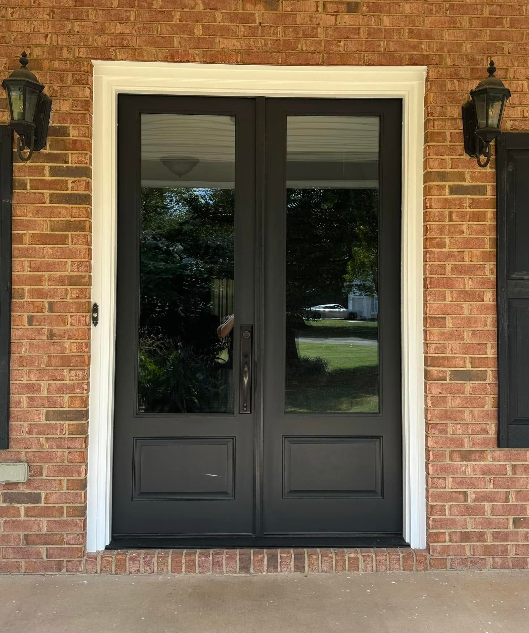 Black double doors with glass panels and white trim on a brick building.