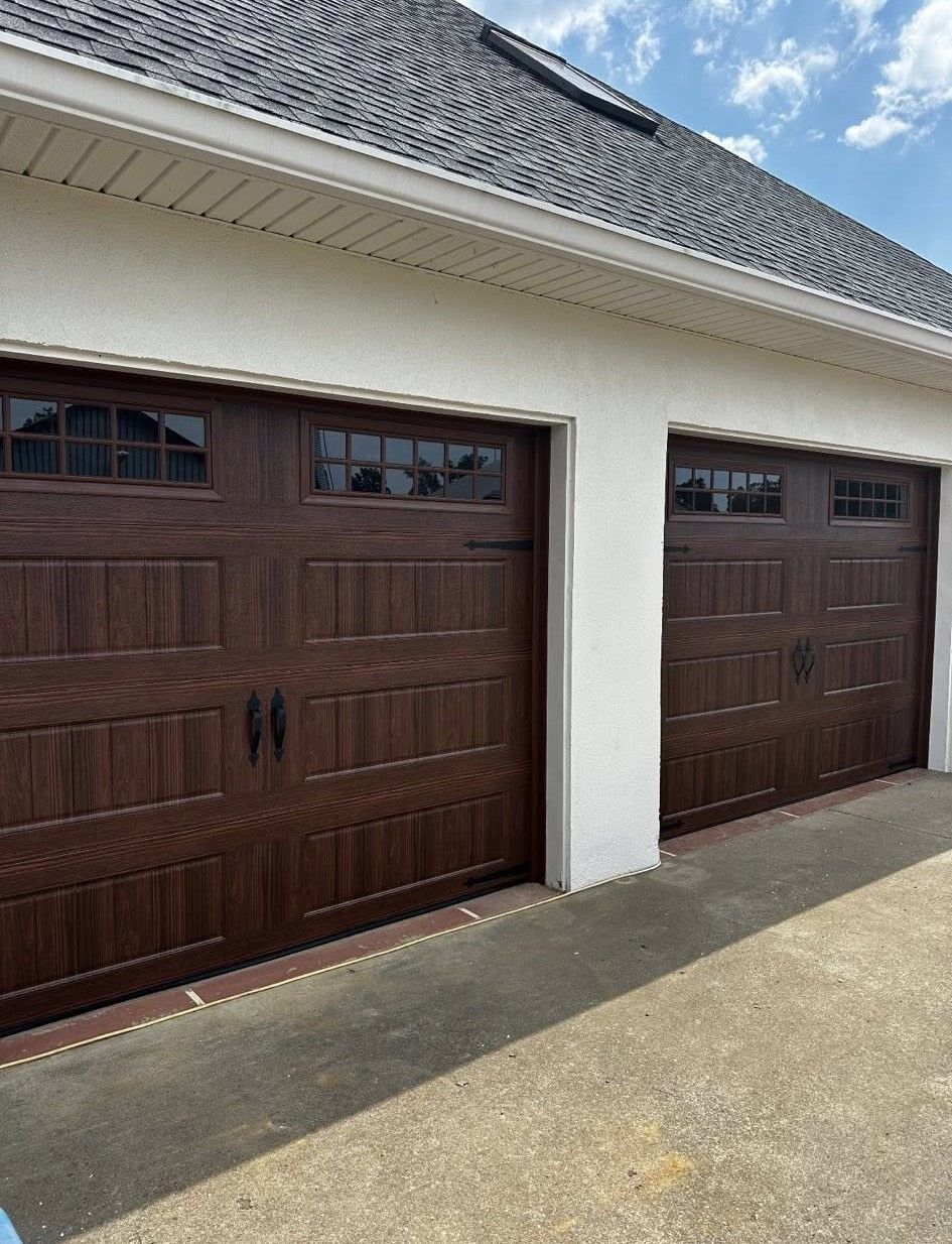 Two brown garage doors with windows, set in a white stucco structure under a dark roof.