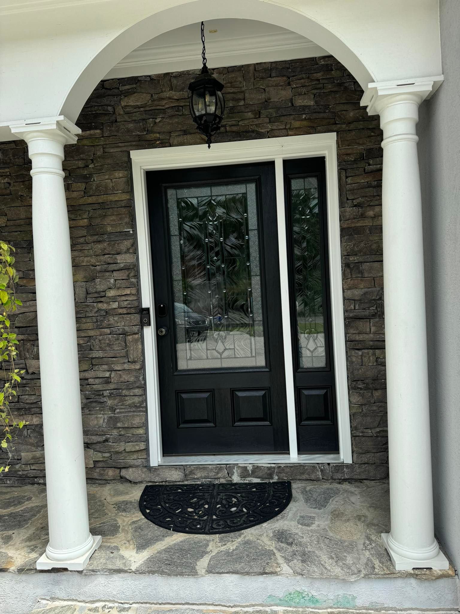 Black door with glass, flanked by sidelight, under a stone archway with white columns.