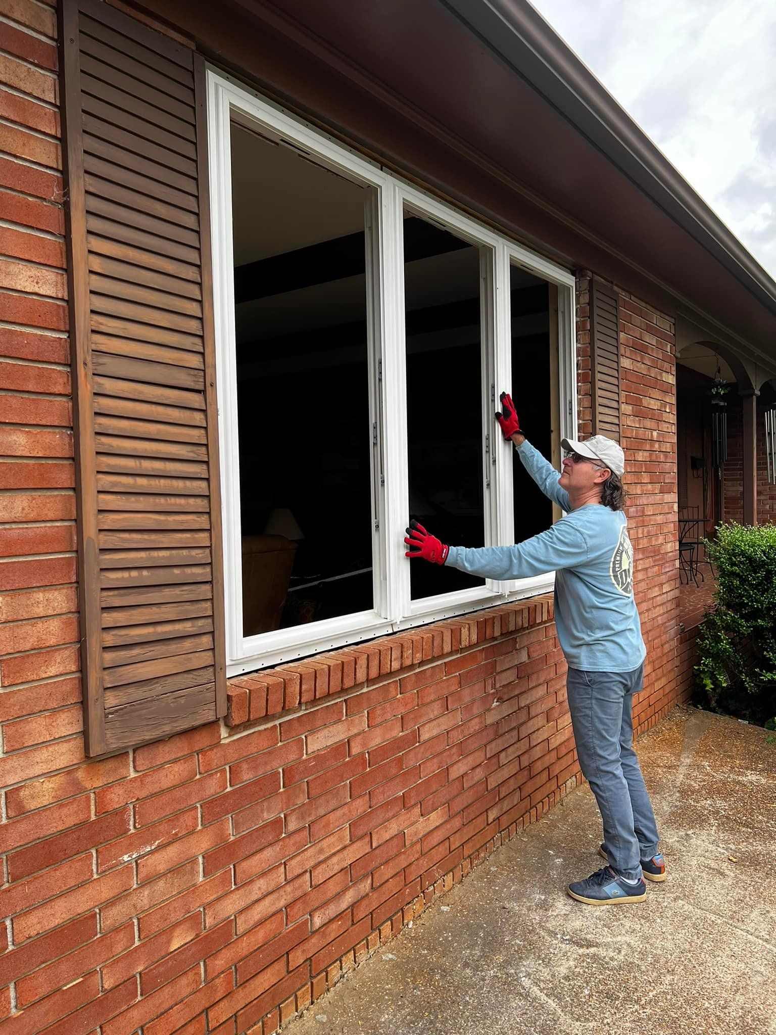 Person wearing a hat and gloves installs a window in a brick house.