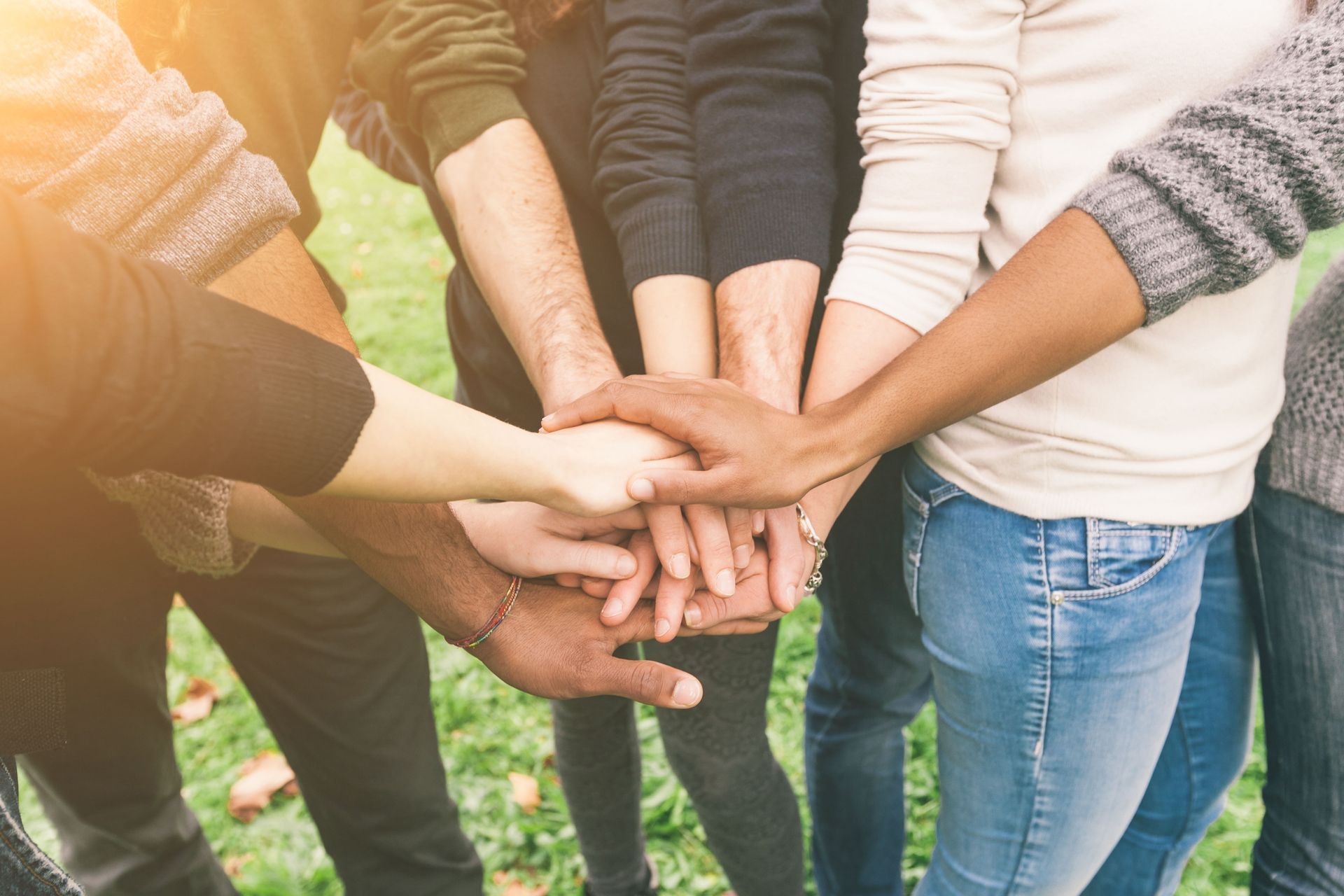 Stacked hands of a group outdoors on grass, symbolizing teamwork