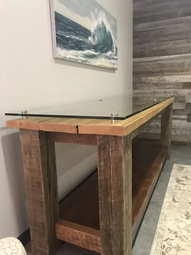A wooden table with a glass top and a painting on the wall above it