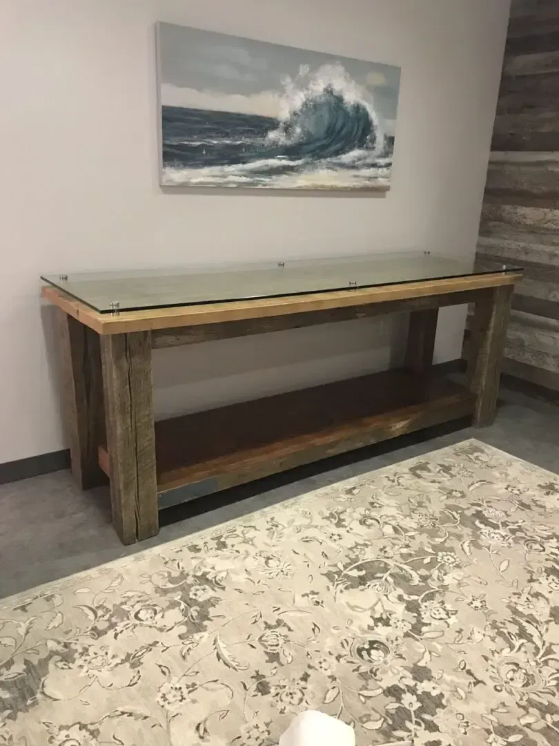A long wooden table with a glass top is sitting in a living room next to a rug.