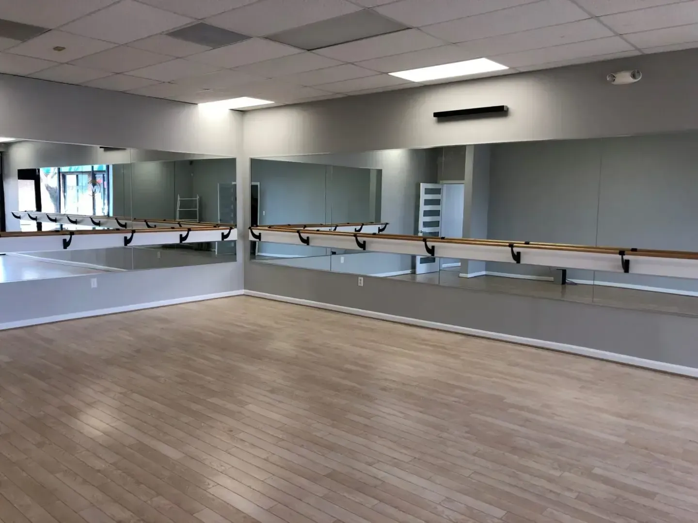 An empty dance studio with a large mirror and a wooden floor.
