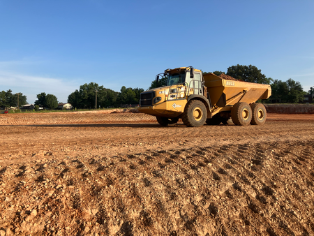 Yellow dump truck on a dirt lot. The truck is in motion, moving across the red soil. Blue sky in the background.