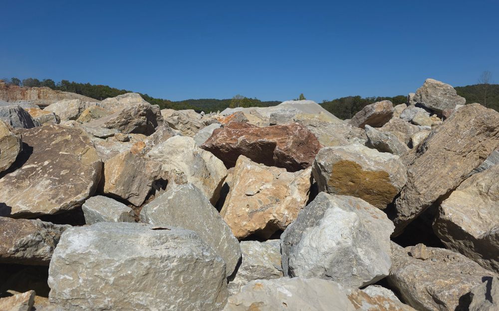 Pile of large, light-colored rocks under a clear blue sky, with a treeline visible in the distance.