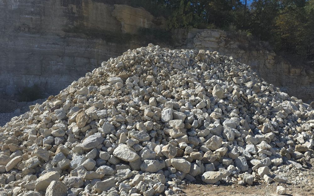 Pile of light-colored rocks, possibly gravel, with a rock quarry background.