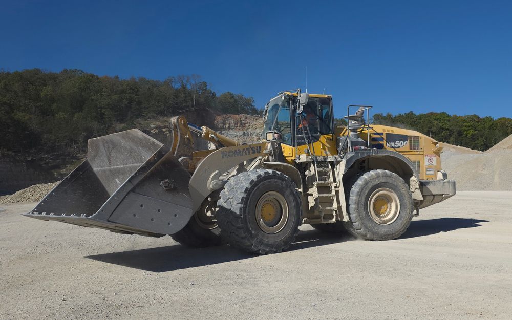 Yellow front-end loader on gravel, scoop down, in quarry setting with blue sky.