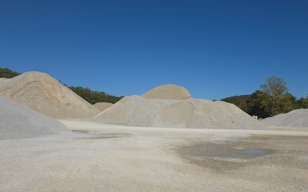 Piles of gravel of varying shades against a blue sky. Gravel pit.