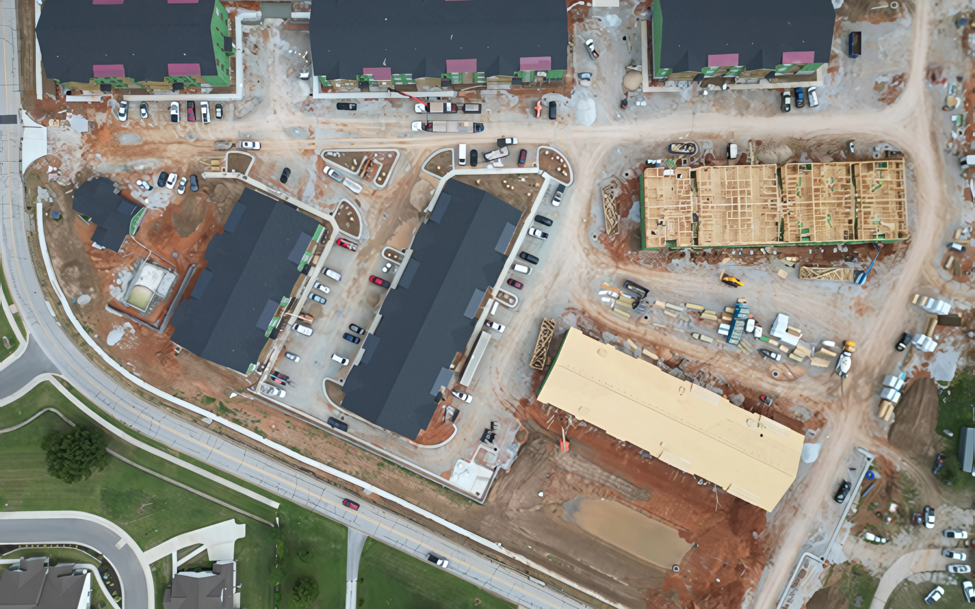 Aerial view of a construction site with buildings, parking areas, and road.