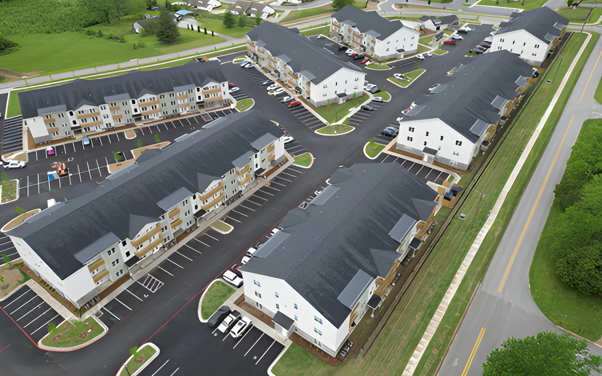 Aerial view of apartment buildings with black roofs, parking lots, and a road.