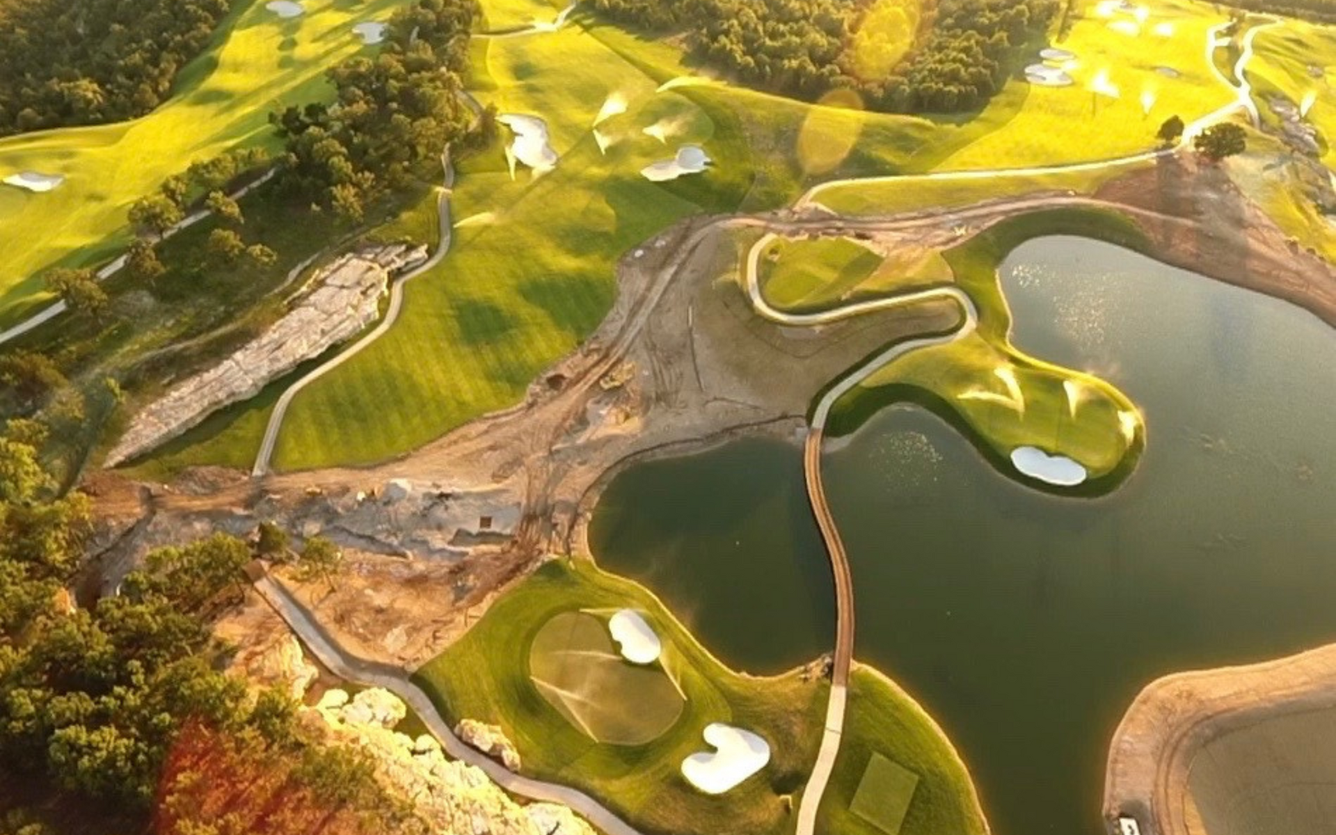 Aerial view of a golf course with green fairways, sand traps, a lake, and a bridge.
