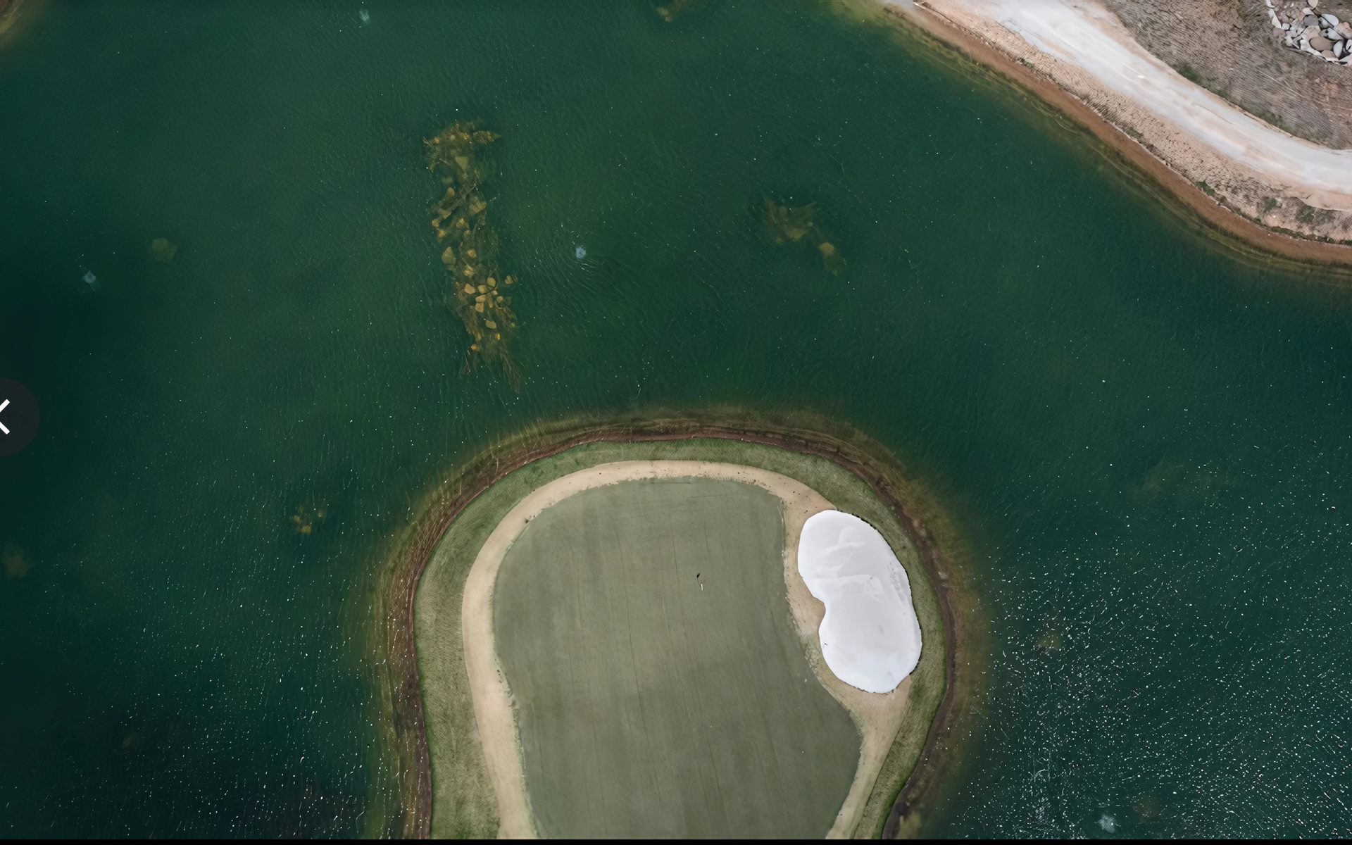 Aerial view of a golf course green surrounded by water, with a white sand trap and a small island.