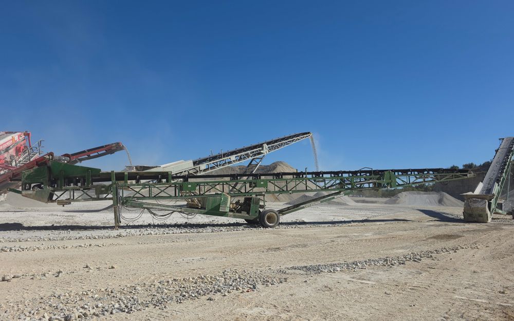 Conveyor belts transporting gravel and rock, on a bright day with a blue sky.