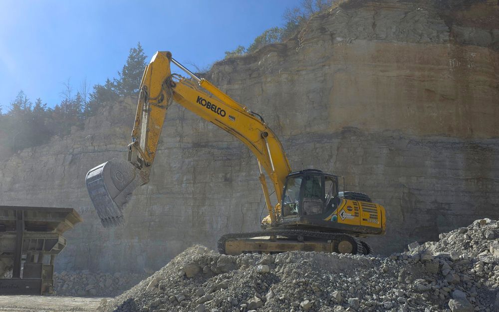 Yellow excavator loading rocks at a quarry on a sunny day.