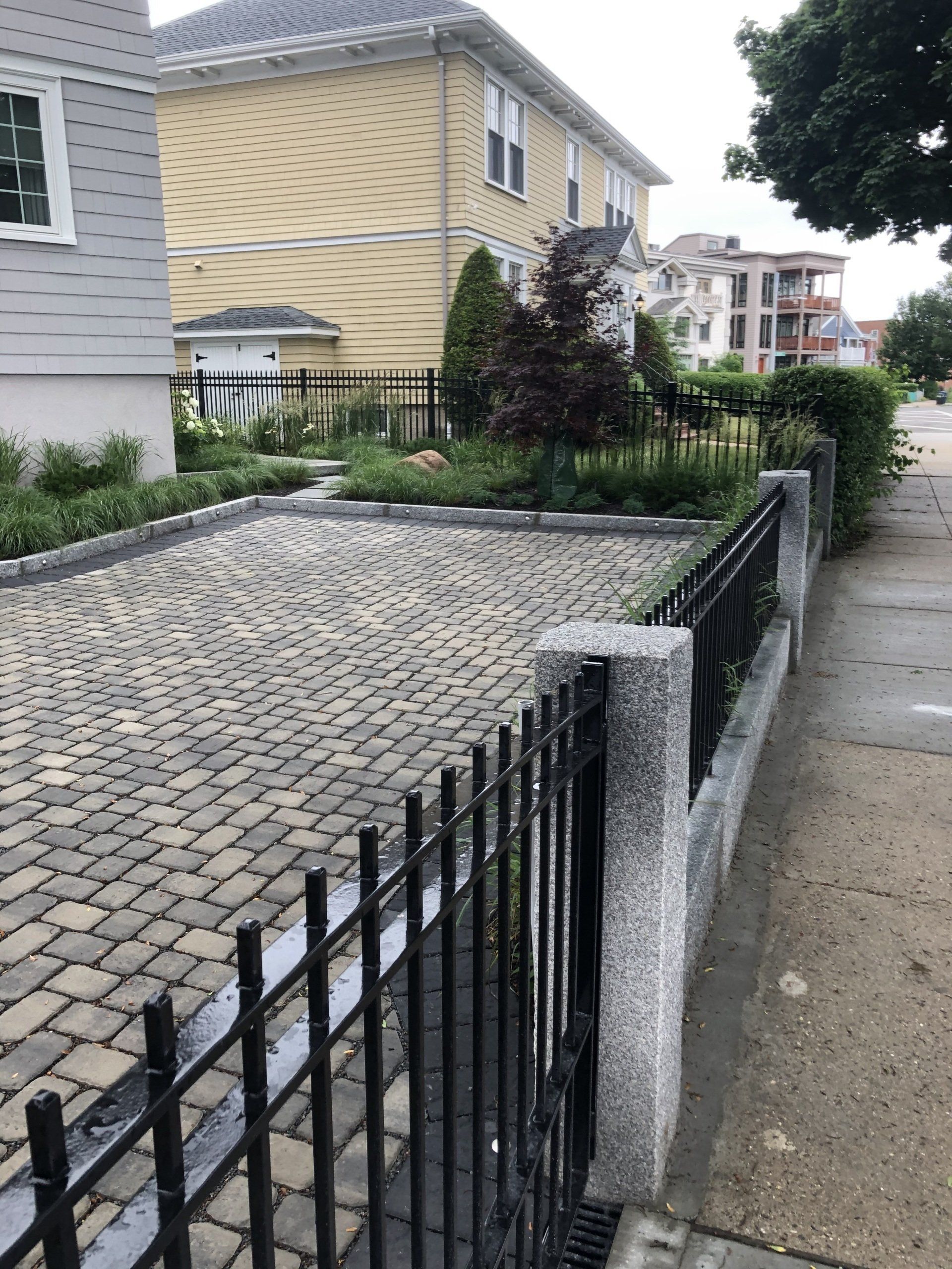 A black fence surrounds a brick driveway in front of a house