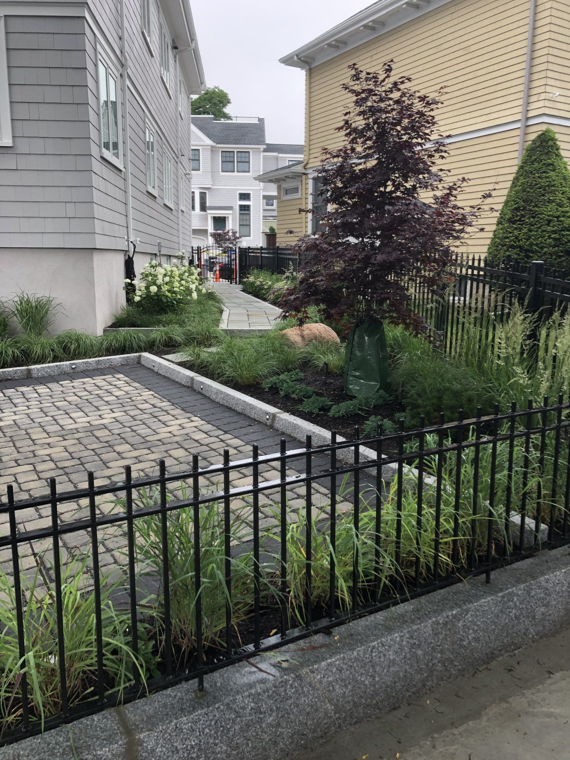A black fence surrounds a garden in front of a house.
