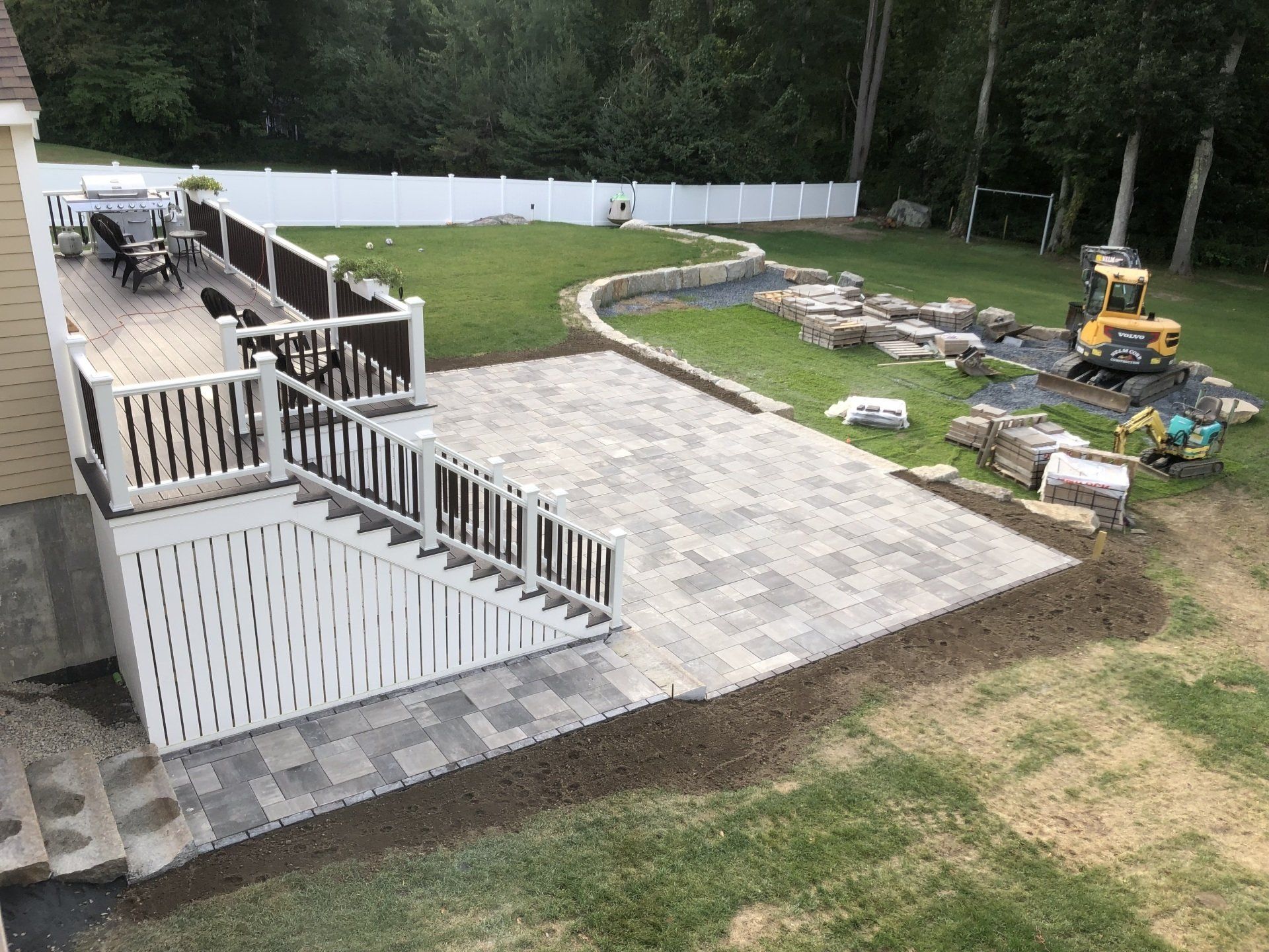 A large patio with a deck and stairs is being built in the backyard of a house.
