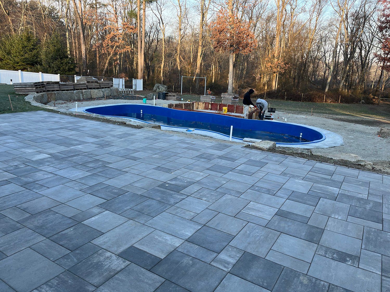 A man is working on a patio next to a swimming pool.