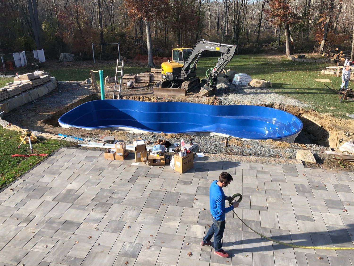 A man is standing on a patio next to a large blue pool.