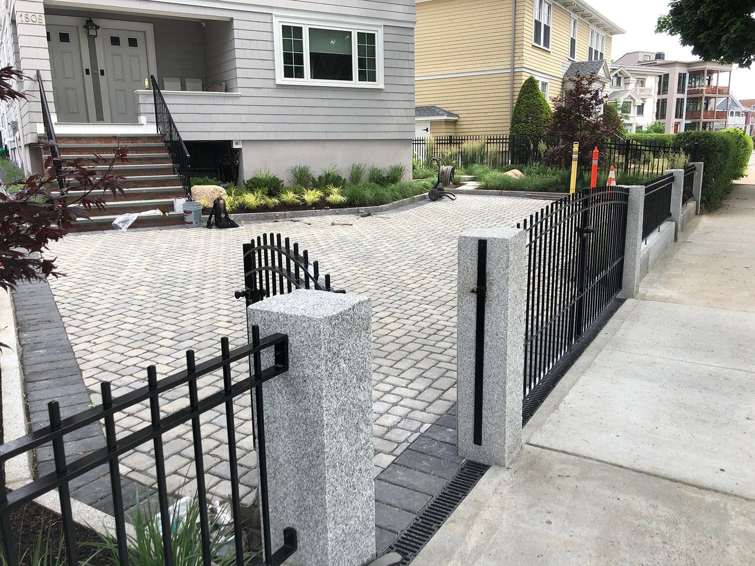 A black fence surrounds a brick driveway in front of a house.