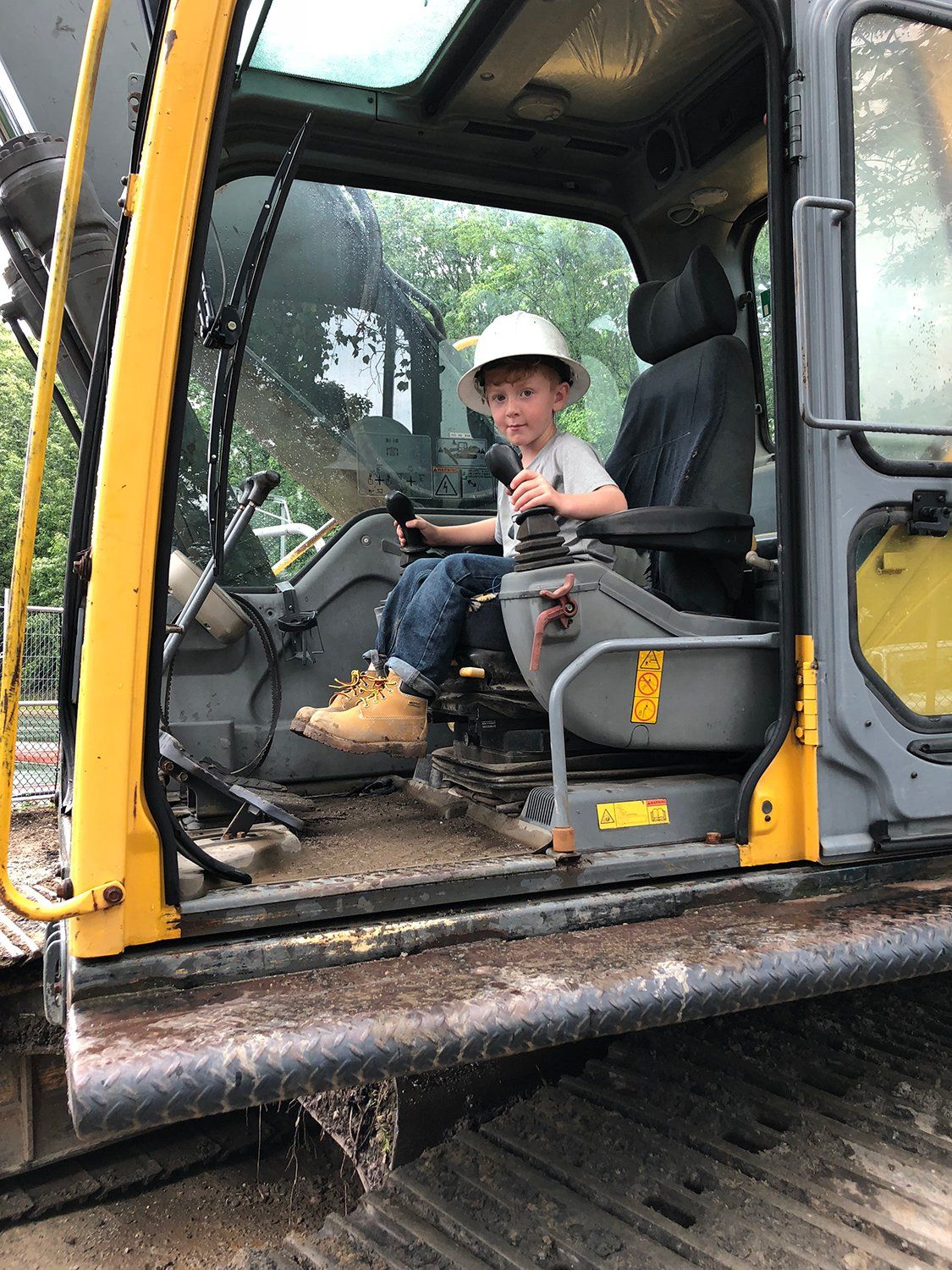 A young boy is sitting in the driver 's seat of an excavator.