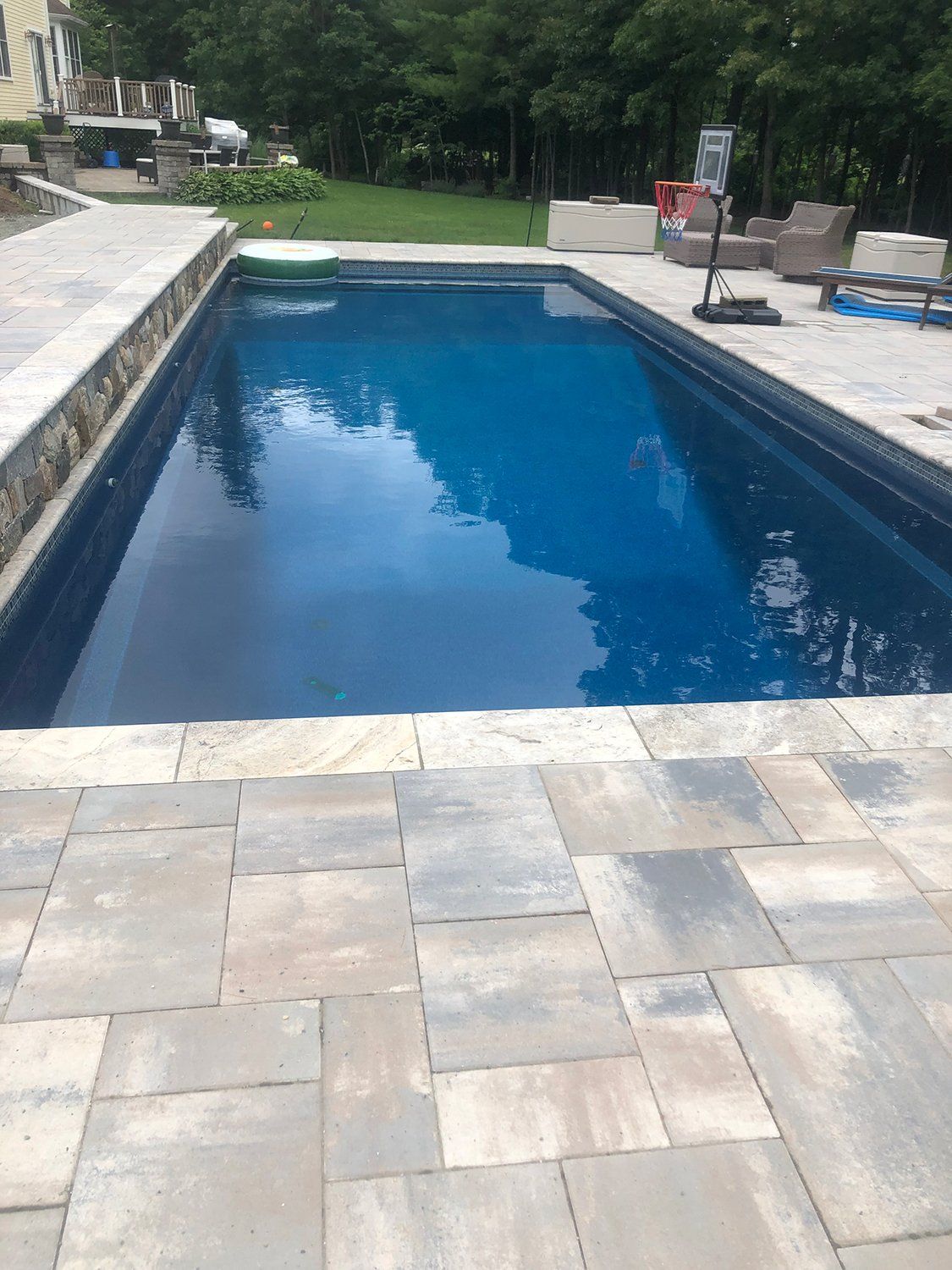 A large swimming pool surrounded by a patio and trees in a backyard.
