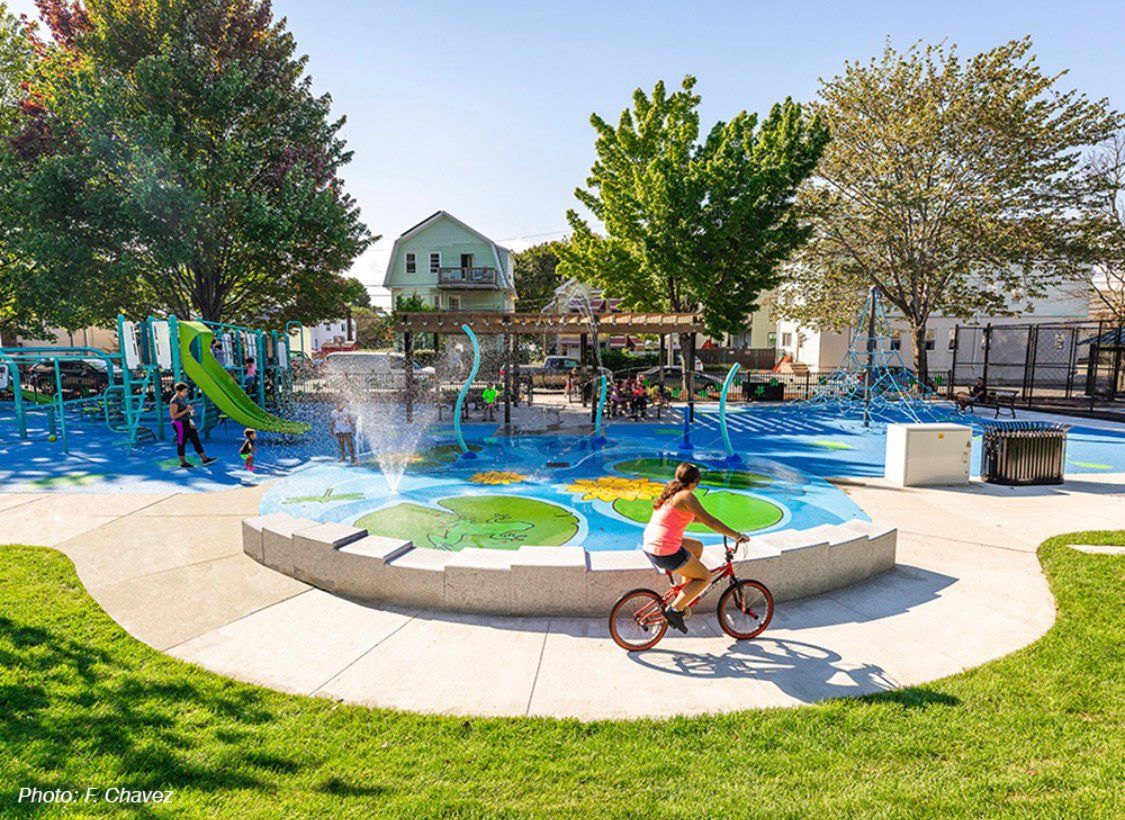 A woman is riding a bike in a park near a fountain.