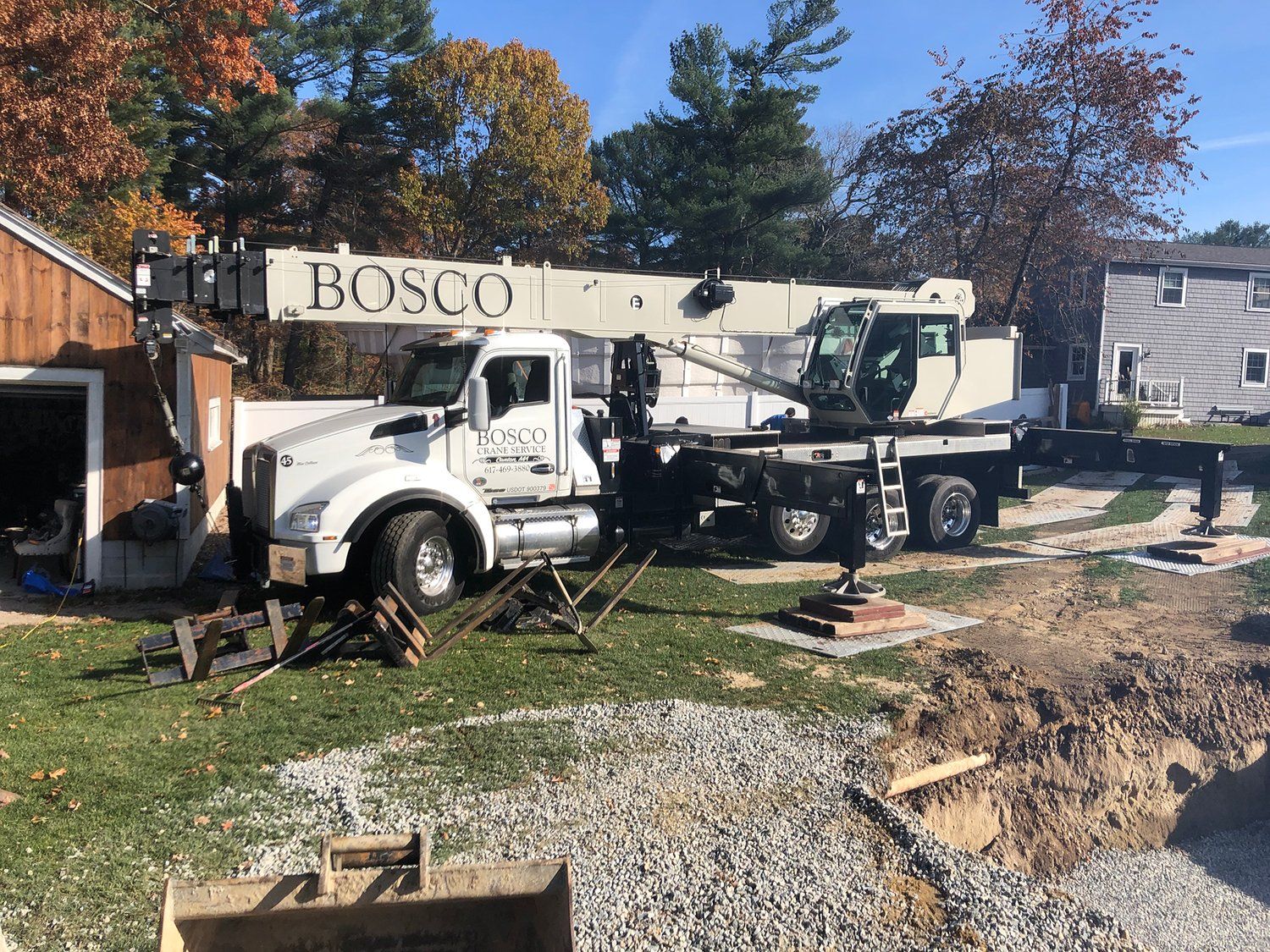 A white truck with a crane attached to it is parked in front of a house.