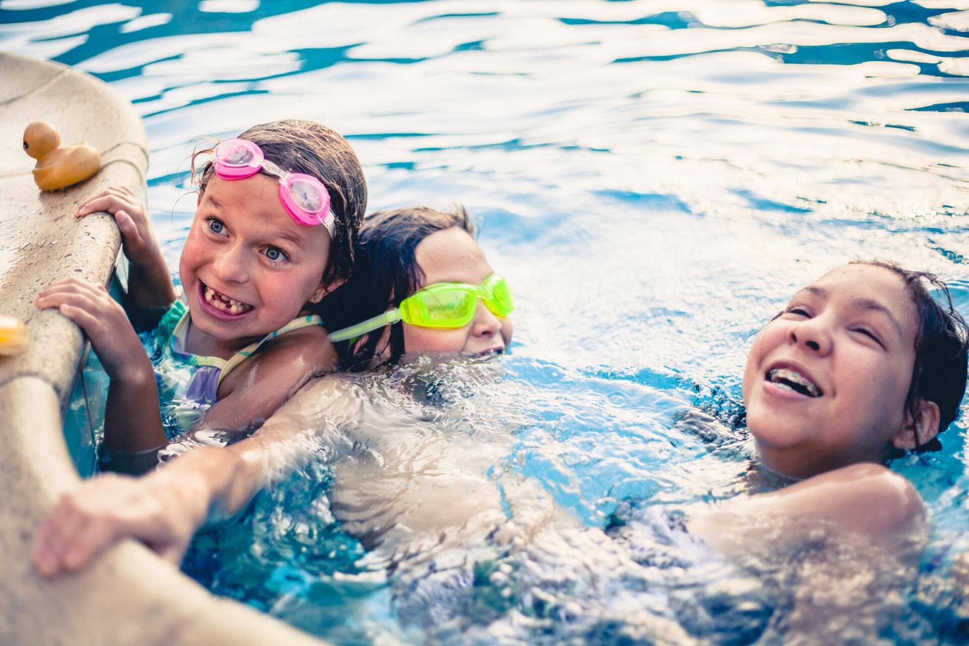 Three young girls are playing in a swimming pool.