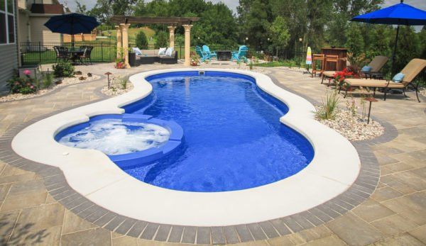 A large blue swimming pool with a hot tub in the middle surrounded by chairs and umbrellas.