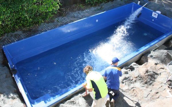 Two men are standing next to a large blue swimming pool.