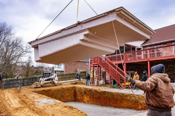 A man is standing in front of a crane lifting a pool into the ground.