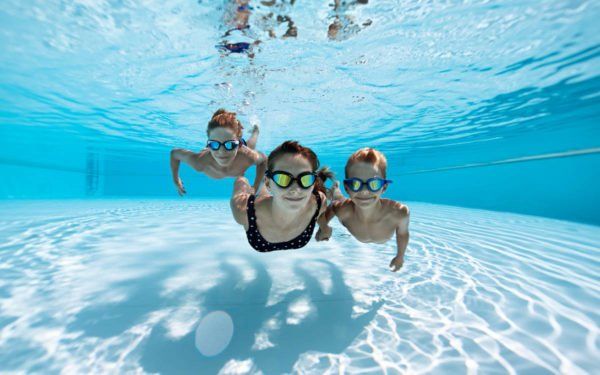A woman and two children are swimming underwater in a swimming pool.