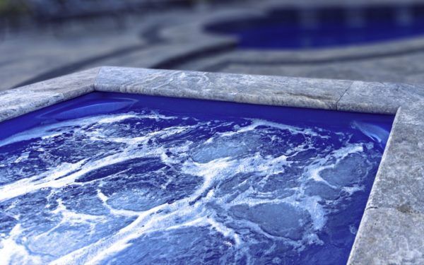 A blue hot tub with bubbles coming out of it is next to a swimming pool.