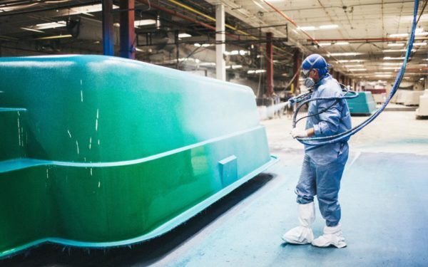A man is painting a green boat in a factory.