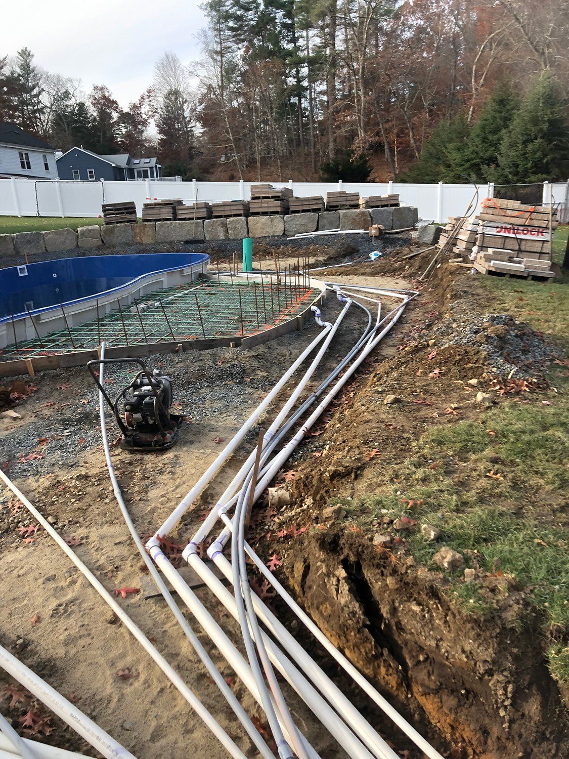 A pile of pipes is sitting in the dirt in front of a swimming pool under construction.