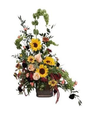Floral arrangement with sunflowers, roses, and greenery in a square, bronze vase.