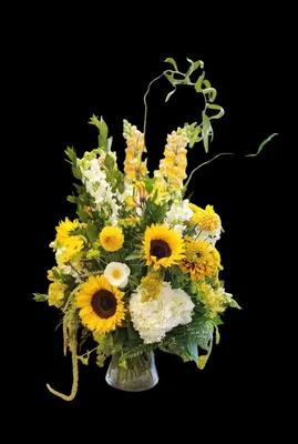 Yellow and white floral arrangement in a vase against a black background.