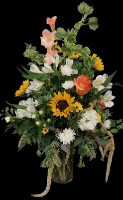 Colorful bouquet of sunflowers, lilies, and other flowers in a clear vase against a black background.