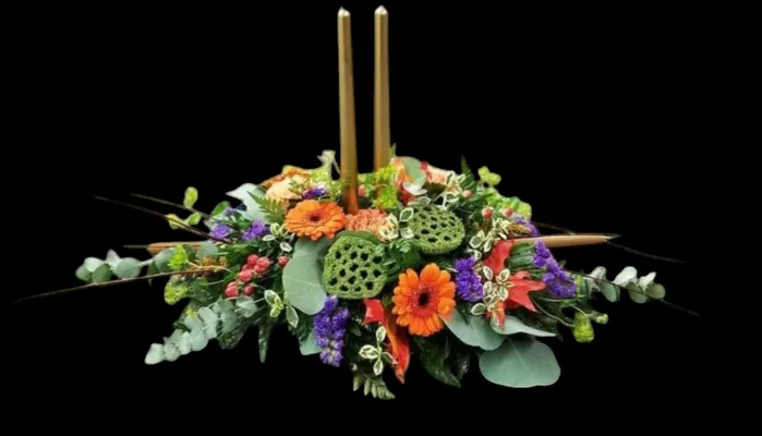 Floral centerpiece with orange and purple flowers, greenery, and two gold candles.