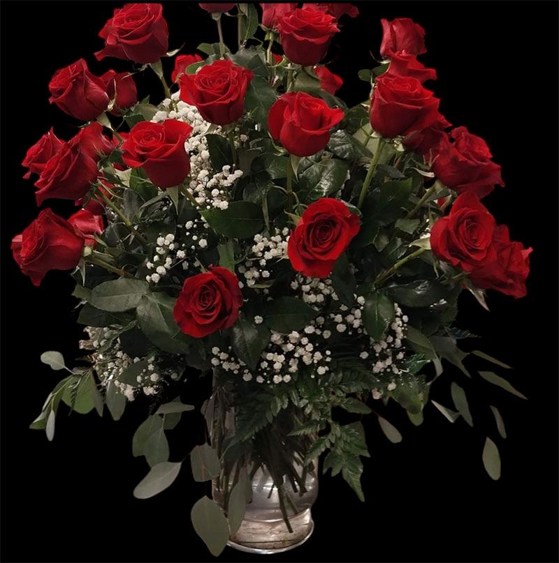 A bouquet of red roses and baby's breath in a glass vase against a black background.
