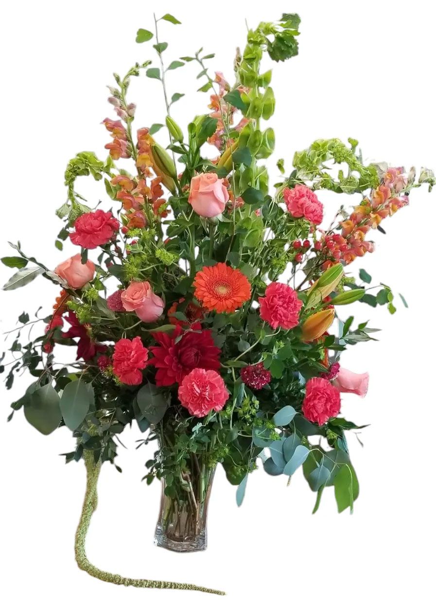 Colorful flower arrangement in a clear vase, featuring roses, carnations, and snapdragons in various shades.