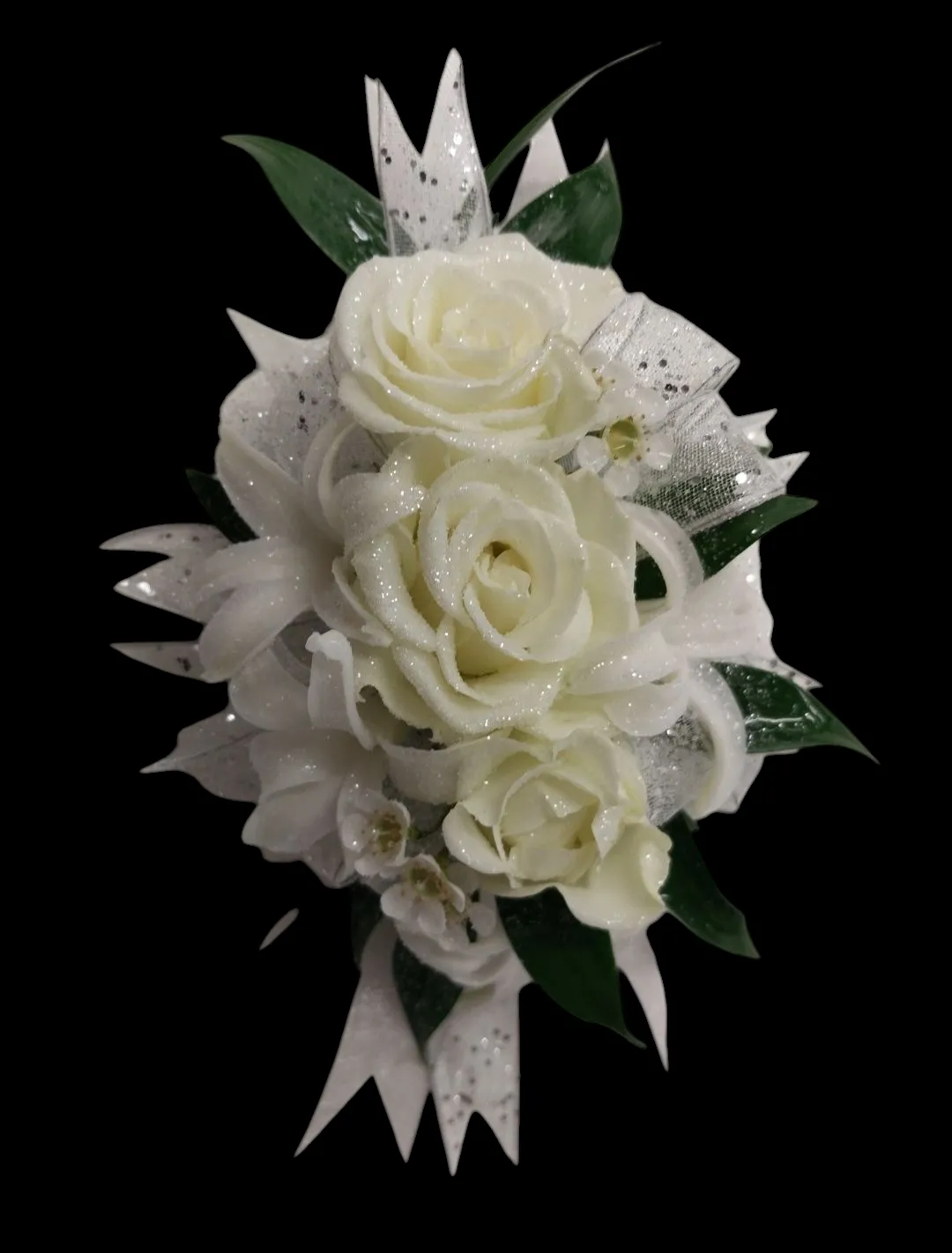 White rose corsage with ribbons and greenery, against a black background.