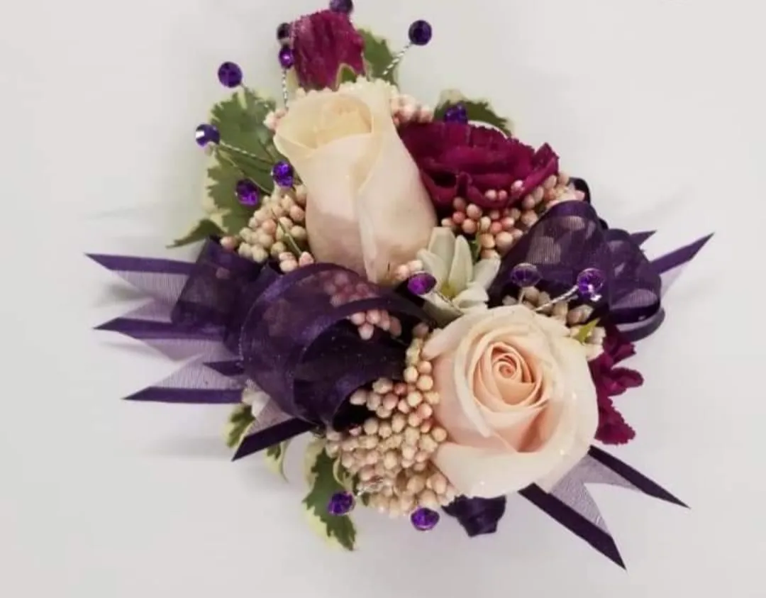 A corsage with light and dark pink roses, purple ribbons, and small white flowers.
