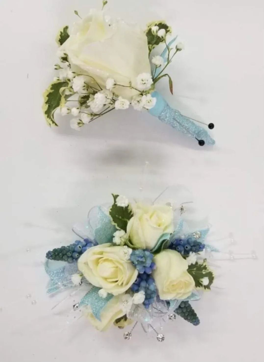 Boutonniere and wrist corsage featuring white roses, baby's breath, and blue accents on a white background.